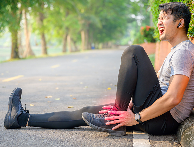 Man sitting on road holding ankle in pain