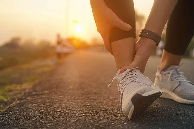 Athlete holding an injured ankle while wearing running shoes