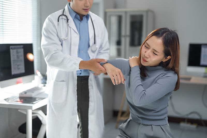 Doctor examining the arm of a young woman experiencing shoulder pain