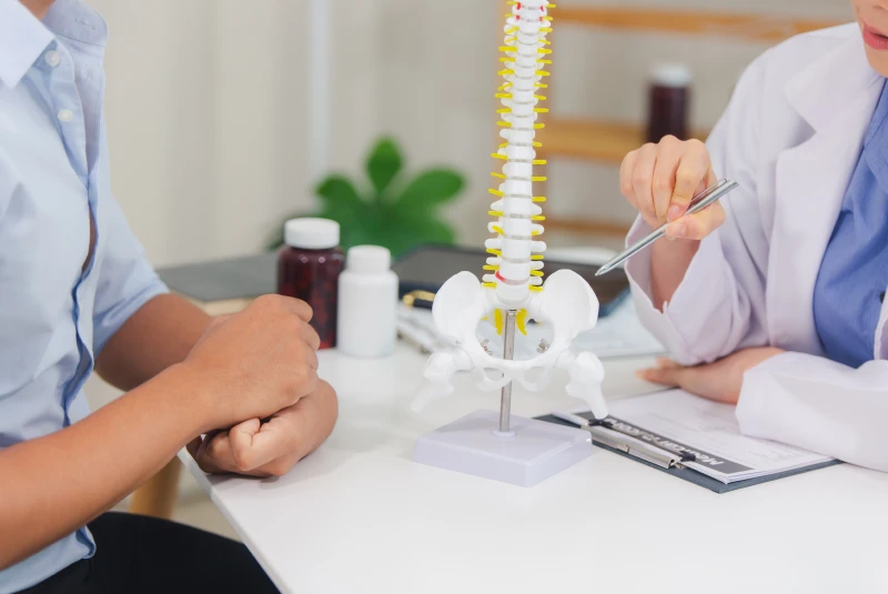 Doctor showing a patient a model of the spine, pointing to the hip.